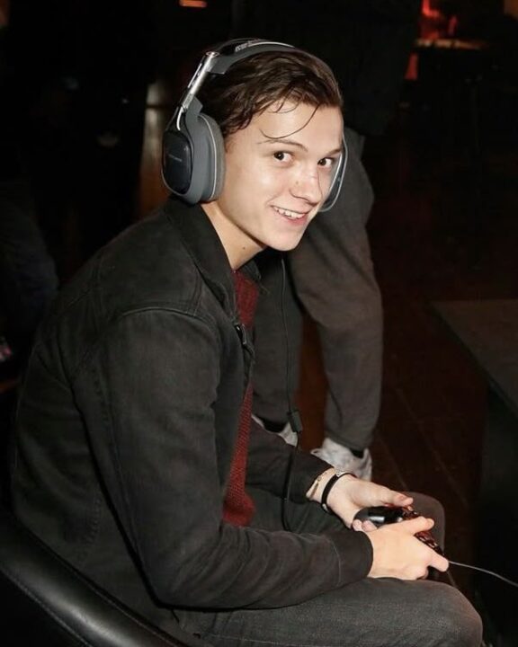 Young Person Wearing Over ear Headphones Smiling While Holding a Game Controller in a Dim Indoor Setting