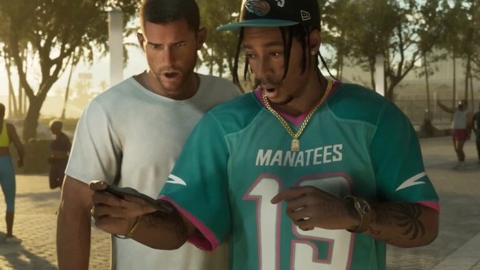 Two men outdoors, one in a teal Manatees jersey #13 looking at a smartphone with the other man closely behind him.