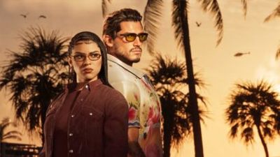 Two stylish adults stand back-to-back at sunset with palm trees in the background, wearing sunglasses and fashionable outfits.