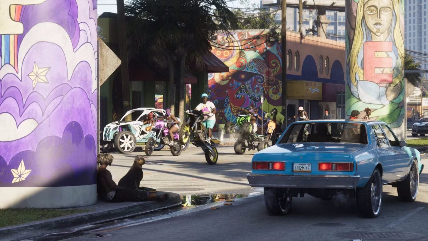Blue Vintage Car Drives Past Colorful Mural covered Pillars As People Ride Motorized Bikes in a Sunny Urban Scene Onlookers Nearby