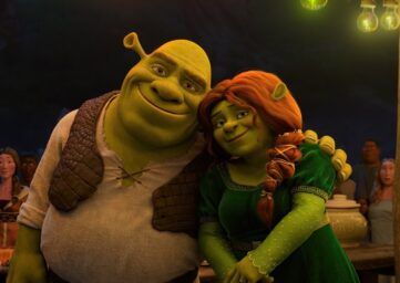 Shrek and Princess Fiona smile together at a nighttime village celebration, with villagers in the background.