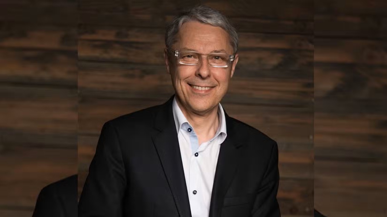 Portrait of claude guillemot Smiling Man in a Dark Suit and Glasses Posing for a Professional Studio Portrait Against a Wooden Backdrop