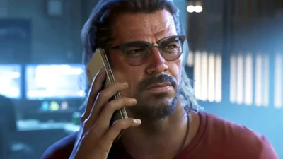 Bearded man with glasses on a phone call in a dim, high-tech control room.