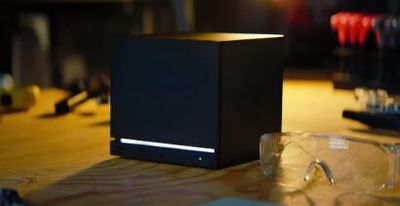 Black computer tower on a wooden table with a blue LED strip, paired with safety glasses in the foreground in a dim, warm-lit setting.