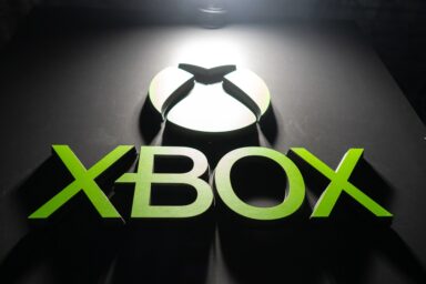 XBOX logo sign in bright green lettering on a dark surface, with a circular light feature above.
