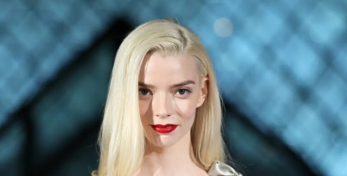 Portrait of a blonde woman with bold red lipstick looking at the camera against a blue bokeh background.