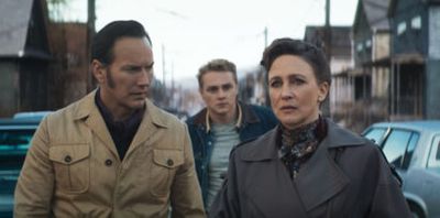 Three adults walk down a vintage-era street; two men flank a worried woman in the foreground.