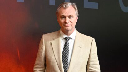 Man in a beige suit and striped tie posing against a dark backdrop at a formal event.