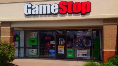 GameStop storefront in a strip mall with posters in the windows and an OPEN sign visible in the door window