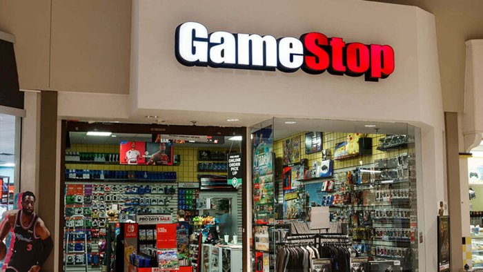GameStop storefront in a mall, glass doors open to a stocked store with video games and accessories visible inside.