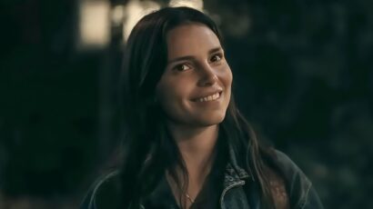 Woman with long dark hair smiling warmly at night, wearing a denim jacket outdoors.