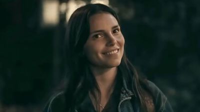 Woman with long dark hair smiling warmly at night, wearing a denim jacket outdoors.