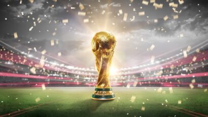 Golden FIFA World Cup trophy on a soccer field with bright stadium lights and falling confetti in celebration.