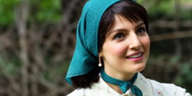 Smiling woman outdoors wearing a teal polka-dot headscarf and matching neck scarf, floral blouse, pearl drop earring.