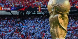 FIFA World Cup trophy in the foreground with a packed stadium and red-clad Spain fans in the background.