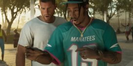 Two men outdoors, one in a teal Manatees jersey #13 looking at a smartphone with the other man closely behind him.