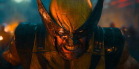 Close-up of a costumed fighter in yellow armor and a jagged helmet, snarling with teeth bared amid warm lighting
