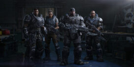 Four heavily armored soldiers in futuristic suits stand with large guns in a dim, industrial workshop setting.